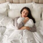 Quelle couette choisir selon la saison ? femme qui sert sa couette agréable